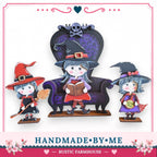three small, cartoonish figures of girls dressed as witches, each holding a broom and a book. They are arranged in a row, with the central figure sitting on a purple chair. The background of the image is white, and there is a heart shape at the top left corner. The image also includes text that reads "HANDMADE BY ME" and "RUSTIC FARMHOUSE".