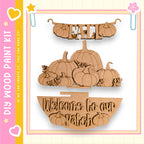 a wooden sign with the word "Fall" written on it, along with a wooden bowl and several wooden pumpkins. The sign is hanging on a wall, and the wooden bowl is placed on the ground. The pumpkins are arranged in a decorative manner, creating a welcoming atmosphere for visitors to the patch.
