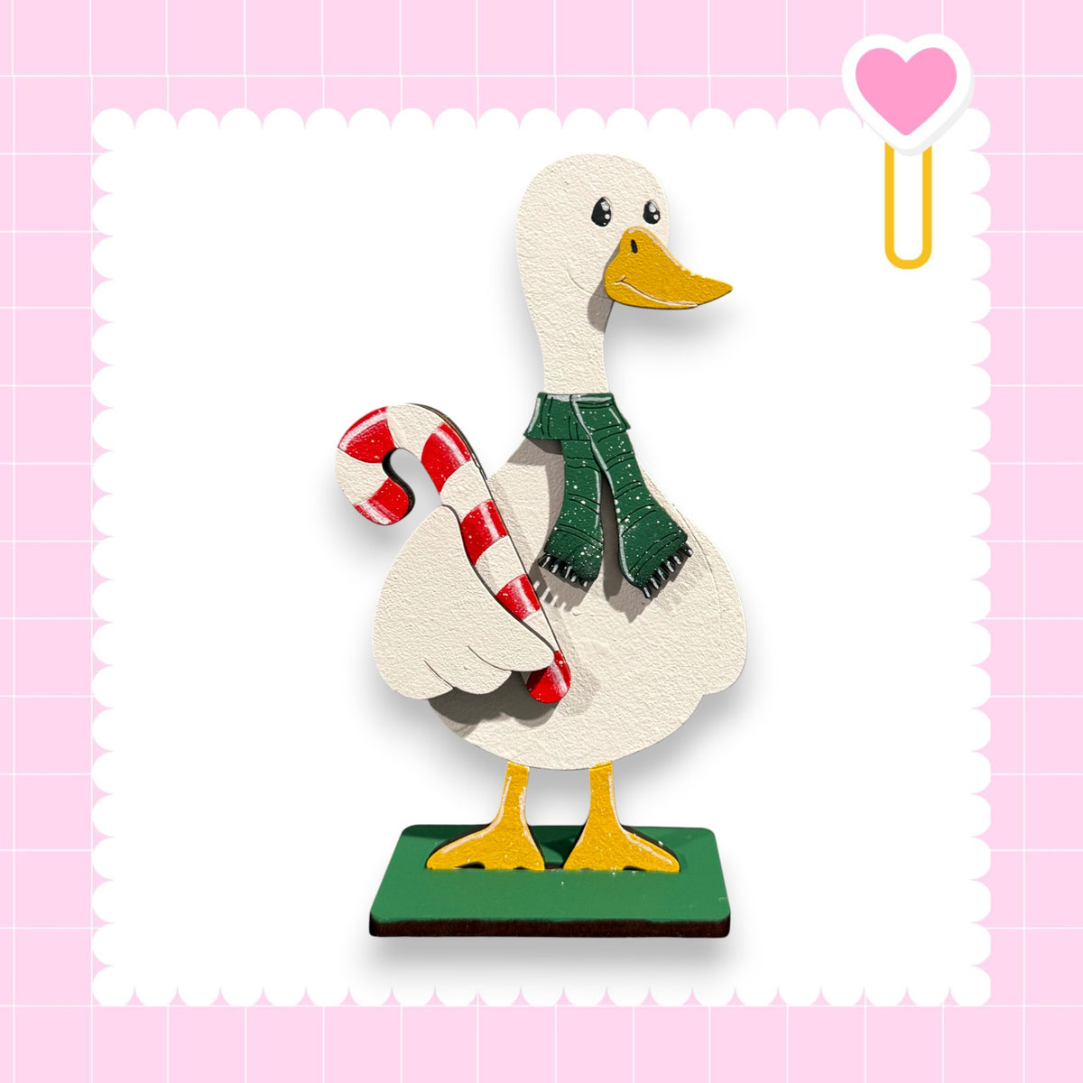 A wooden duck statue wearing a green scarf and holding a red and white striped candy cane.