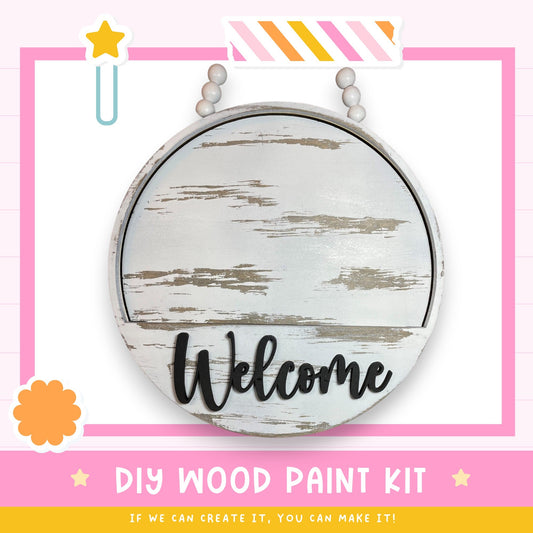 a DIY wood paint kit with a welcome sign, a star, and a flower. The kit appears to be made of wood and is designed for creating a welcome sign.