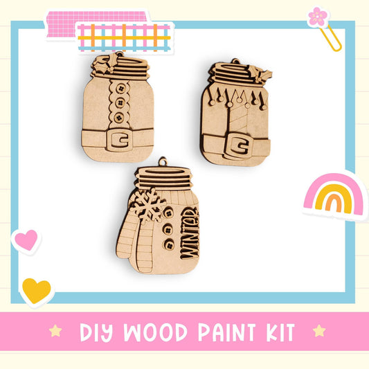 The image is a DIY wood paint kit featuring three wooden ornaments, including a mason jar, a snowman, and a rainbow.