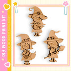 three wooden cutouts of girls wearing witch hats, each holding a different object, such as a book and a wand.