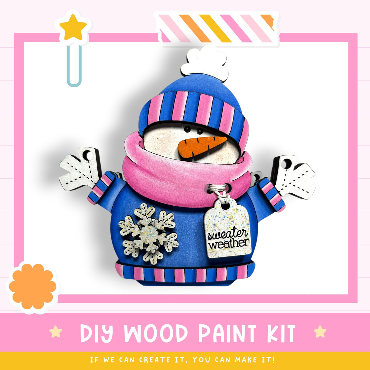 A wooden snowman figure wearing a pink and blue striped sweater and a blue hat with a white stripe, holding a carrot and wearing a "sweater weather" tag. The image is framed by a pink border with a yellow star and a white cloud.