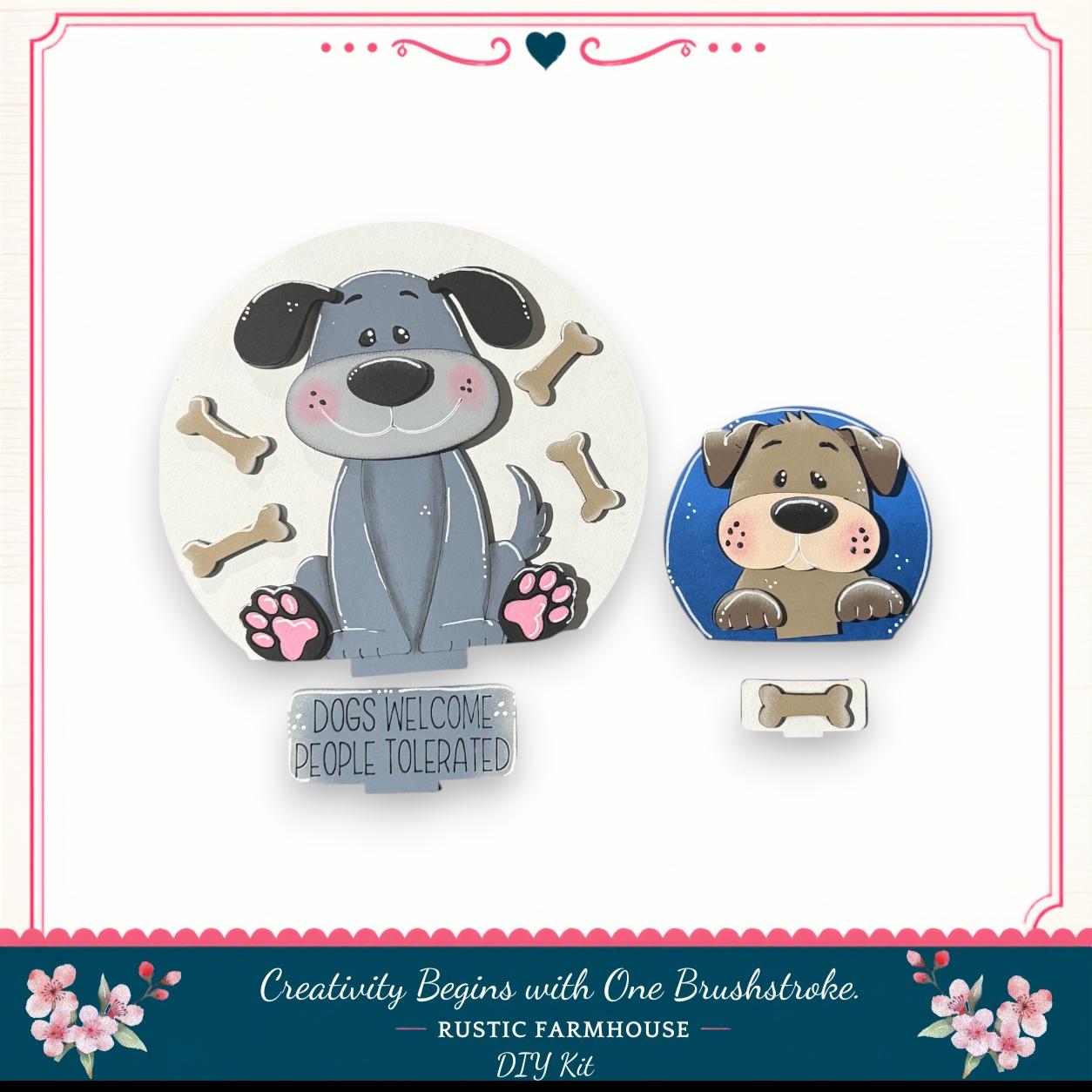 two cartoon dog illustrations, one larger and one smaller, surrounded by dog bones. The larger dog is sitting on a sign that says "Dogs Welcome People Tolerated", and the smaller dog is peeking out from behind a blue frame. The image is described as a "DIY Kit" and "Creativity Begins with One Brushstroke" from a "RUSTIC FARMHOUSE".