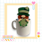 A cartoon mug with a smiling face and a clover leaf, set against a grid background with various colorful stickers.