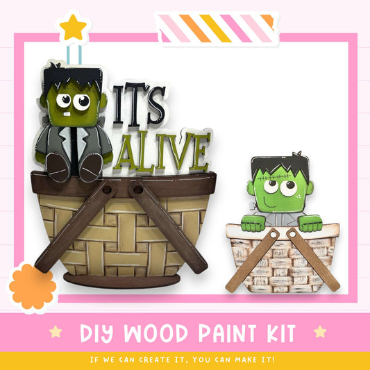 two green monster characters sitting in a basket, with the text "IT'S ALIVE" displayed above them. The image also includes a DIY wood paint kit and a motivational message encouraging creativity.