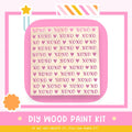 The image is a promotional poster for a DIY wood paint kit. It features a pink background with a repeating pattern of the word "XOXO" in various sizes and colors. The text "DIY WOOD PAINT KIT" is prominently displayed, along with the phrase "IF WE CAN CREATE IT, YOU CAN MAKE IT!" at the bottom of the image.