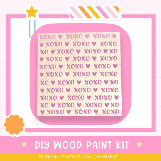 The image is a promotional poster for a DIY wood paint kit. It features a pink background with a repeating pattern of the word "XOXO" in various sizes and colors. The text "DIY WOOD PAINT KIT" is prominently displayed, along with the phrase "IF WE CAN CREATE IT, YOU CAN MAKE IT!" at the bottom of the image.