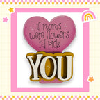 a heart-shaped sign with the text "If moms were flowers I'd pick you" written on it, along with the word "YOU" in a larger font. The sign is surrounded by a pink border and is set against a background with a checkered pattern.