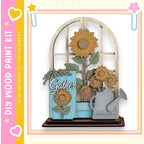 A wooden paint kit featuring a decorative arrangement of sunflowers and a watering can, with the word "Gather" written on the blue piece.