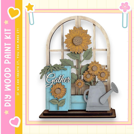 A wooden paint kit featuring a decorative arrangement of sunflowers and a watering can, with the word "Gather" written on the blue piece.