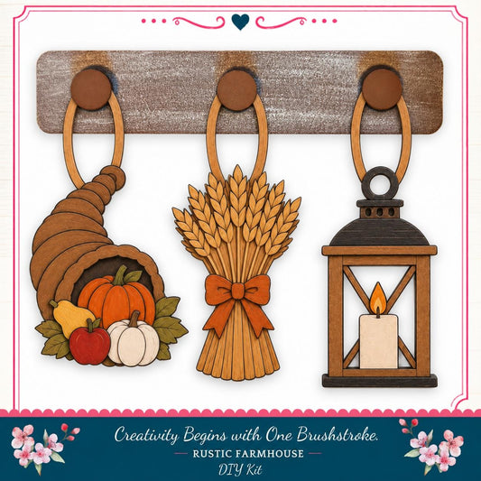 a rustic farmhouse-style DIY kit with three wooden ornaments hanging on a wooden board. The ornaments include a carved wooden cornucopia, a bundle of wheat, and a lantern with a lit candle.