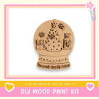A wooden snow globe with a Christmas tree and a bear, along with the text "Have yourself a Merry little Christmas" and "DIY WOOD PAINT KIT"
