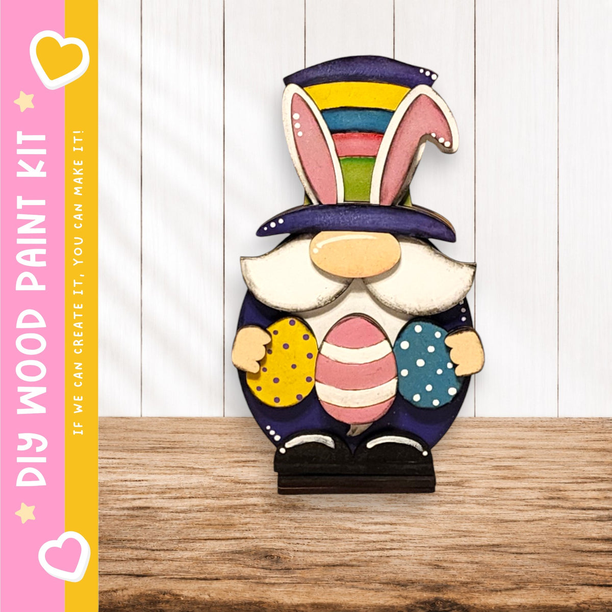 A wooden gnome figurine holding Easter eggs, wearing a colorful hat, stands on a wooden surface against a white background.