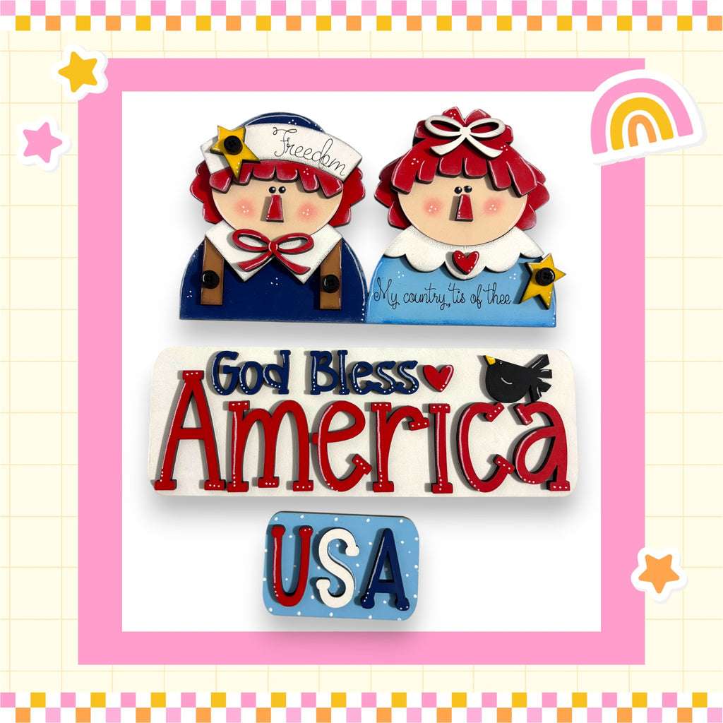 two cartoon-style dolls, one wearing a blue outfit and the other in a red outfit, with the text "God Bless America" and "USA" displayed prominently.