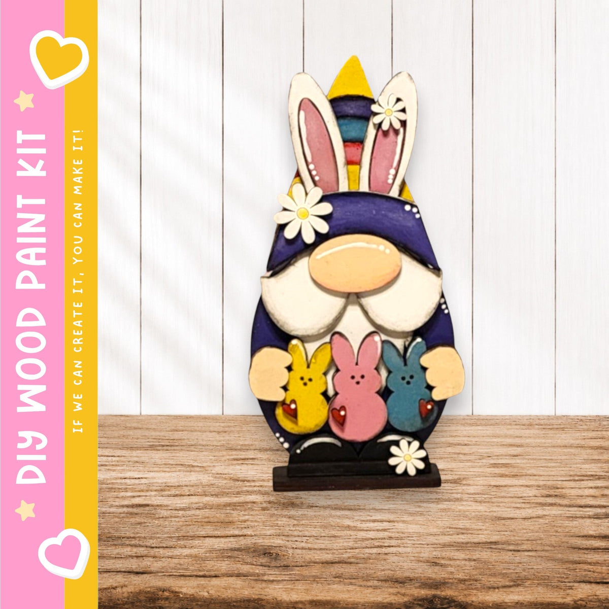A wooden gnome figurine holding three colorful Easter bunny plush toys, set against a white wooden background.