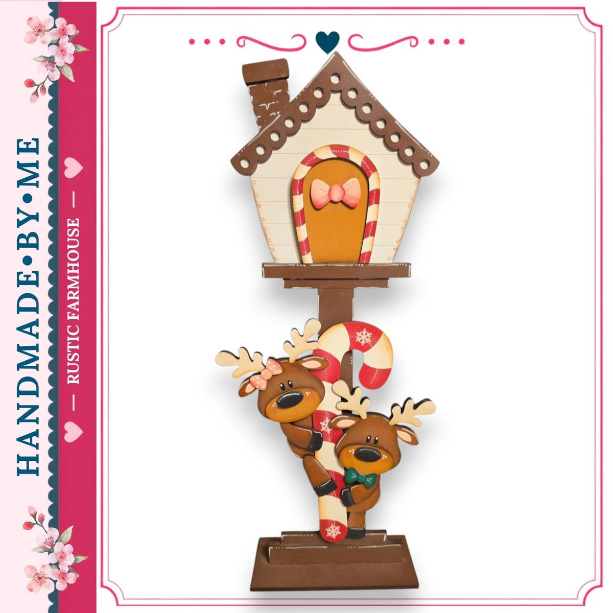 A hand-made wooden ornament featuring a gingerbread house with a bow, decorated with two reindeer and a candy cane.