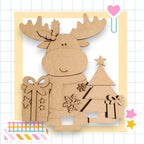 A cardboard cutout of a smiling moose holding a gift box and a Christmas tree, set against a grid background with a heart and stars.