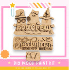 The image is a promotional poster for a DIY wood paint kit, featuring three wooden cutouts of ghost characters and the text "Boo Crew" and "Spookytown Home of the Boo".