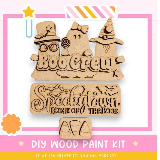 The image is a promotional poster for a DIY wood paint kit, featuring three wooden cutouts of ghost characters and the text "Boo Crew" and "Spookytown Home of the Boo".