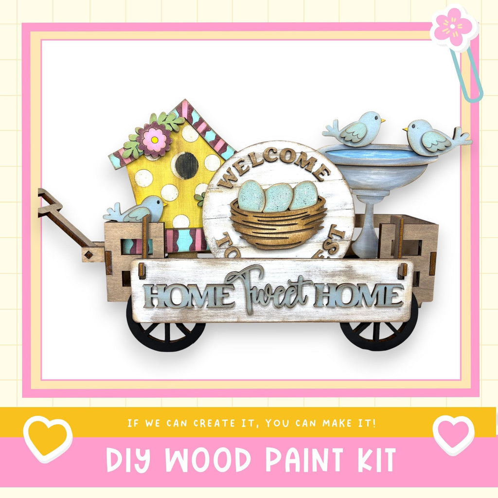a DIY wood paint kit for creating a "Home Sweet Home" sign. The sign is made of wood and includes a birdhouse, a bird bath, and a sign that says "Welcome Home". The kit is presented in a wooden cart, and the text "If we can create it, you can make it!" is displayed.