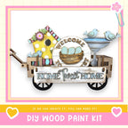 a DIY wood paint kit for creating a "Home Sweet Home" sign. The sign is made of wood and includes a birdhouse, a bird bath, and a sign that says "Welcome Home". The kit is presented in a wooden cart, and the text "If we can create it, you can make it!" is displayed.