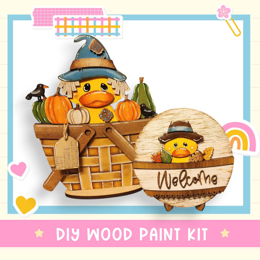 a DIY wood paint kit for creating a wooden basket with a whimsical design, including a duck wearing a witch's hat and holding a basket filled with pumpkins and a sign that says "Welcomhe".