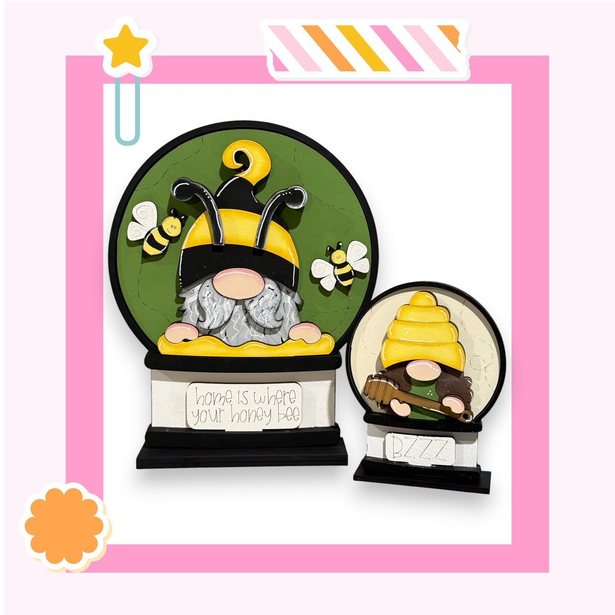 two gnomes, one larger and one smaller, both wearing yellow hats and holding honeycombs. The larger gnome is positioned in the center of the image, while the smaller gnome is located to the right. The background of the image is green, and there is a sign that reads "home is where your honey bee" in the bottom left corner.