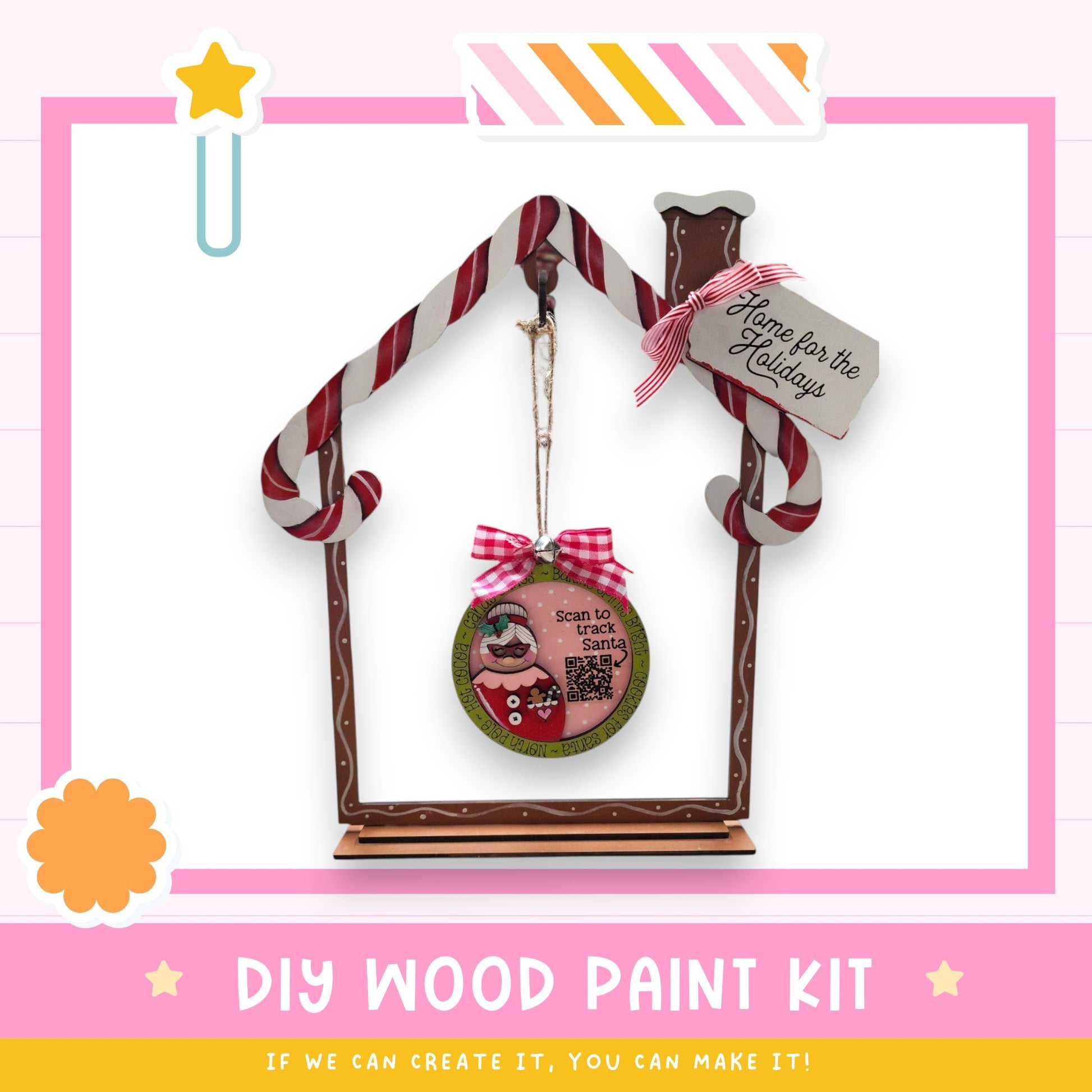 a DIY wood paint kit for creating a wooden ornament in the shape of a house. The kit includes a wooden frame, a candy cane decoration, and a sign that says "Home for the Holidays". The kit is presented in a pink and white color scheme, with a star decoration on the left side. The text "DIY WOOD PAINT KIT" is displayed at the bottom of the image, along with the phrase "If we can create it, you can make it!"