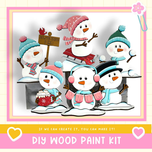 A group of five colorful snowmen, each with unique accessories and clothing, are depicted in a cheerful winter scene. The snowmen are arranged in a row, with one on the left, one in the center, one on the right, and one on the far right. The background is a simple white, and the image includes text that reads "If we can create it, you can make it!" and "DIY WOOD PAINT KIT".