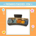 a decorative hair clip with a pumpkin and leaf design on it, surrounded by a colorful border with stars and hearts.
