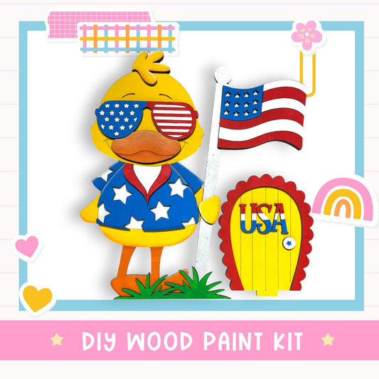 a wooden toy duck wearing sunglasses and holding an American flag, along with a wooden door labeled "USA". The image also includes a "DIY WOOD PAINT KIT" label.