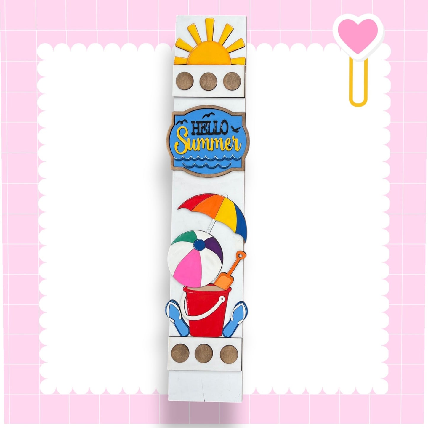 A colorful and playful sign with the text "Hello Summer" and various summer-themed illustrations, including a beach umbrella, bucket, and shovel, all set against a pink background.