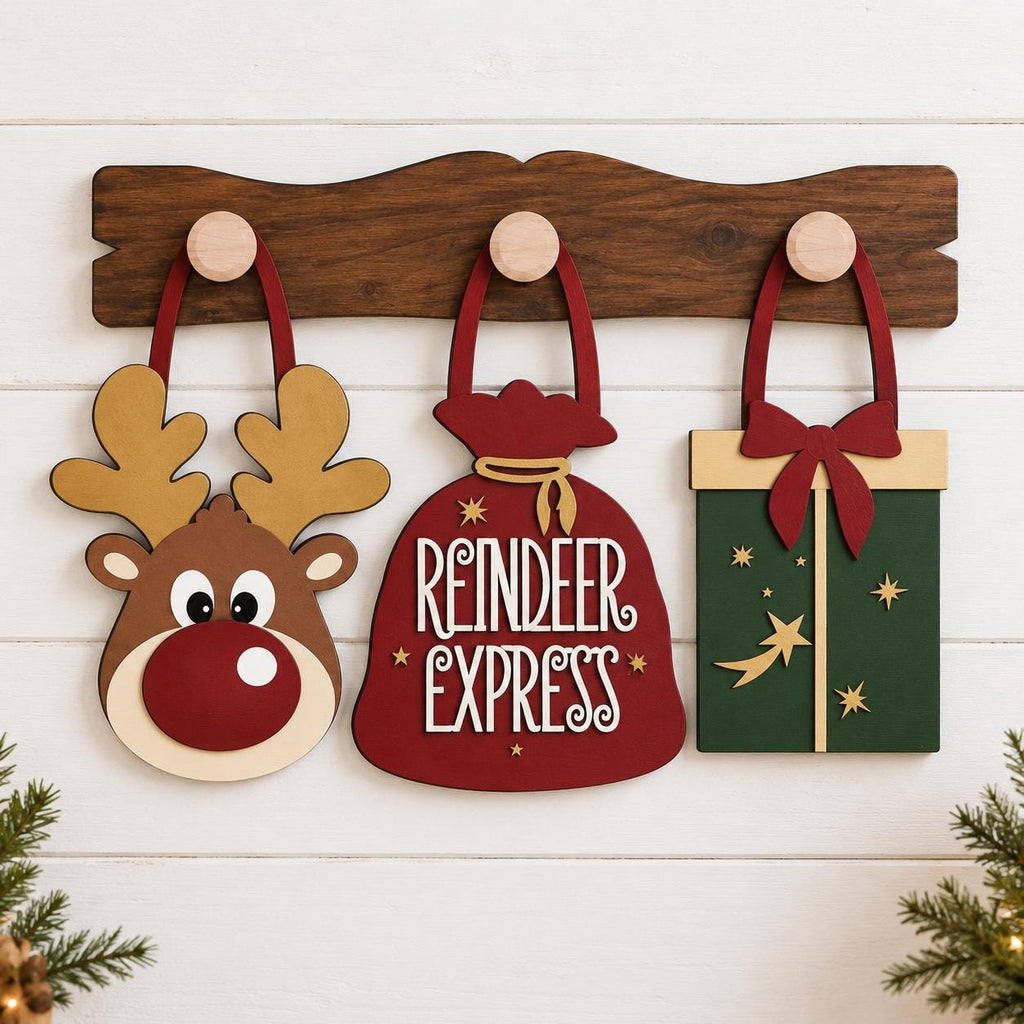 A wooden board with three festive holiday-themed ornaments hanging on it. The first ornament is a reindeer head, the second is a red gift bag with the text "Reindeer Express", and the third is a green gift box with a star design.