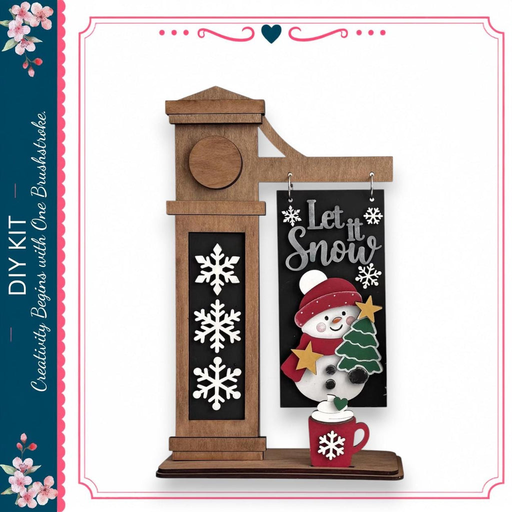A wooden clock with a snowman decoration on it, along with a sign that says "Let it snow".