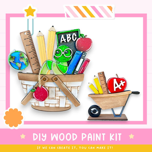 a DIY wood paint kit with various school supplies, including a basket filled with pencils, books, and an apple, as well as a smaller wooden cart with a red apple on top. The kit appears to be made of wood and is designed for children to create their own educational materials.