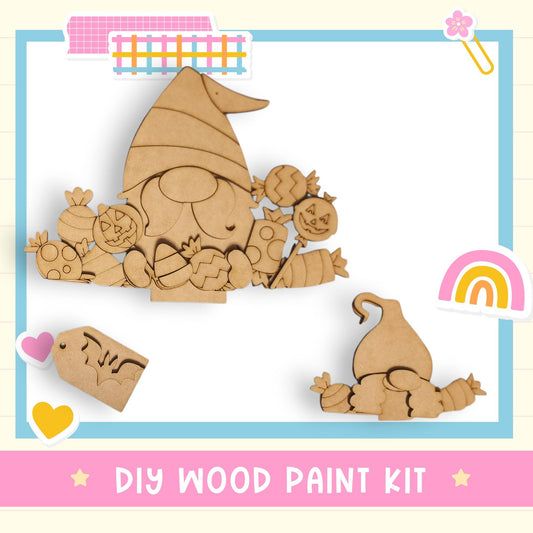 The image is a DIY wood paint kit featuring a wooden gnome and various Halloween-themed items, including a pumpkin and a rainbow.