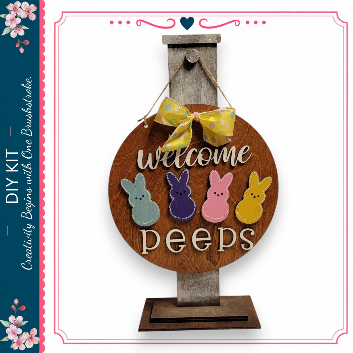 a wooden sign with the words "Welcome Peeps" written on it, hanging on a wooden stand. The sign has four different colored Easter bunny shapes, including a blue bunny, a pink bunny, a purple bunny, and a yellow bunny. The sign is displayed against a white background, and there is a decorative border around the edges.