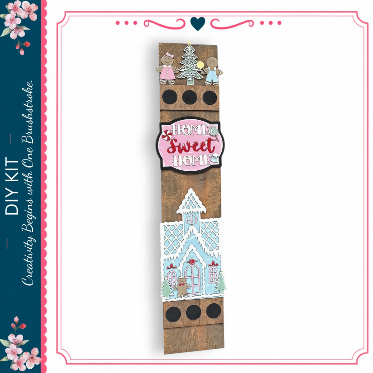 a wooden sign with a winter theme, including a gingerbread house and snowflakes. The sign has a pink and white color scheme and displays the text "Home Sweet Home" in a decorative font.