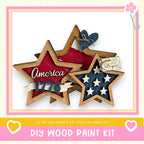 The image is a DIY wood paint kit featuring a wooden star-shaped decoration with the word "America" written on it, along with a heart-shaped decoration. The kit appears to be made of wood and is designed for creating similar star-shaped decorations.