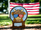 A wooden figurine of a cow wearing sunglasses and an American flag in the background.