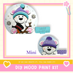 The image is a collage featuring two cute teddy bear designs, one wearing a blue hat and the other wearing a purple hat, both with snowflakes on them. The collage is framed by a pink border and includes text that reads "Mini DIY WOOD PAINT KIT" and "If we can create it, you can make it!"