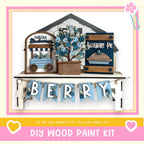 The image is a DIY wood paint kit for creating a wooden sign or decoration with the word "Berry" written on it. The sign is made of wood and features a blueberry pie and a blueberry tree as part of the design. The kit includes the necessary materials and instructions for creating a similar wooden sign or decoration.