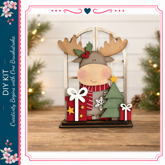 A wooden deer figurine with a Christmas tree and presents sits on a wooden surface, surrounded by holiday decorations and greenery.