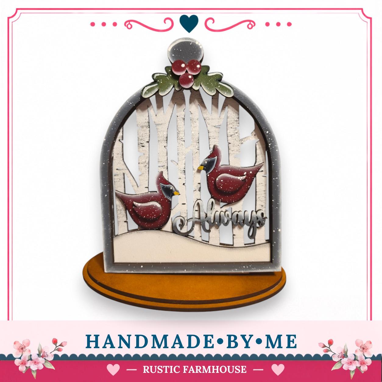 A handcrafted wooden snow globe with a decorative border, featuring two red birds and the phrase "Always" written on it.