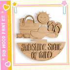 The image is a wooden paint kit featuring a sun and various beach-related items, such as a hat, sunglasses, and a beach bag.