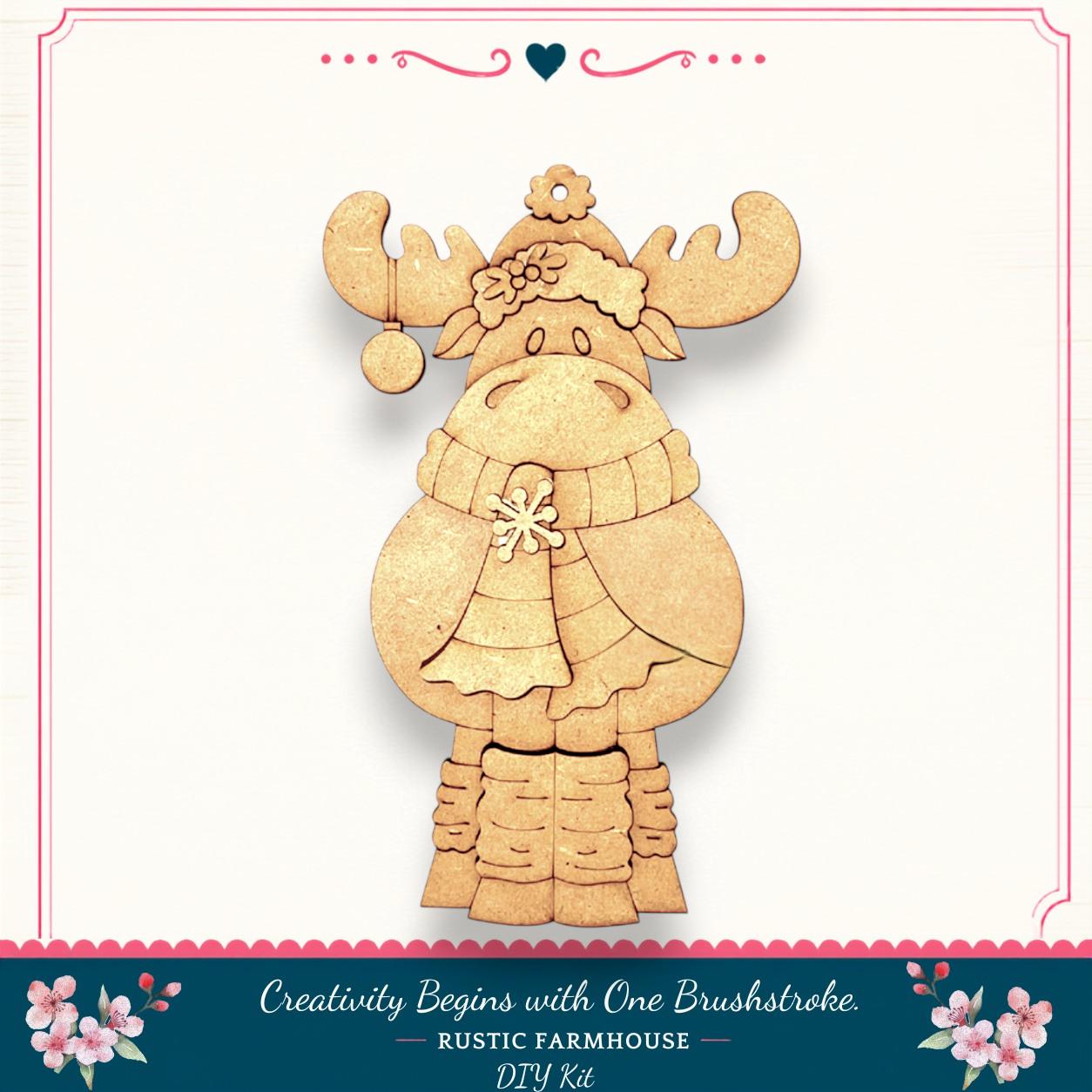 A wooden ornament in the shape of a moose, wearing a scarf and hat, is displayed against a white background.
