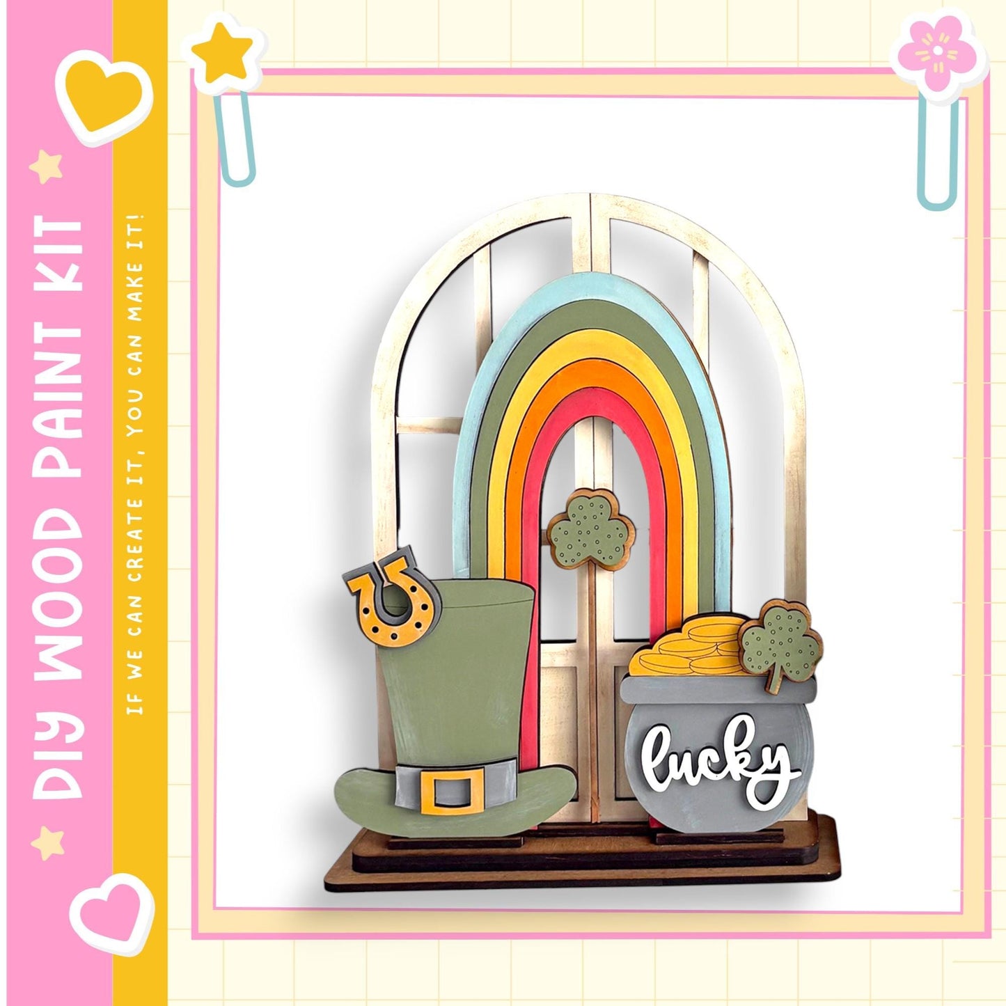A colorful and whimsical wooden craft kit featuring a rainbow, a pot of gold coins, and a hat, all set against a pink and yellow background.