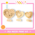 three wooden heart-shaped decorations, each with a unique design and inscription, displayed on a white background within a pink and yellow frame.