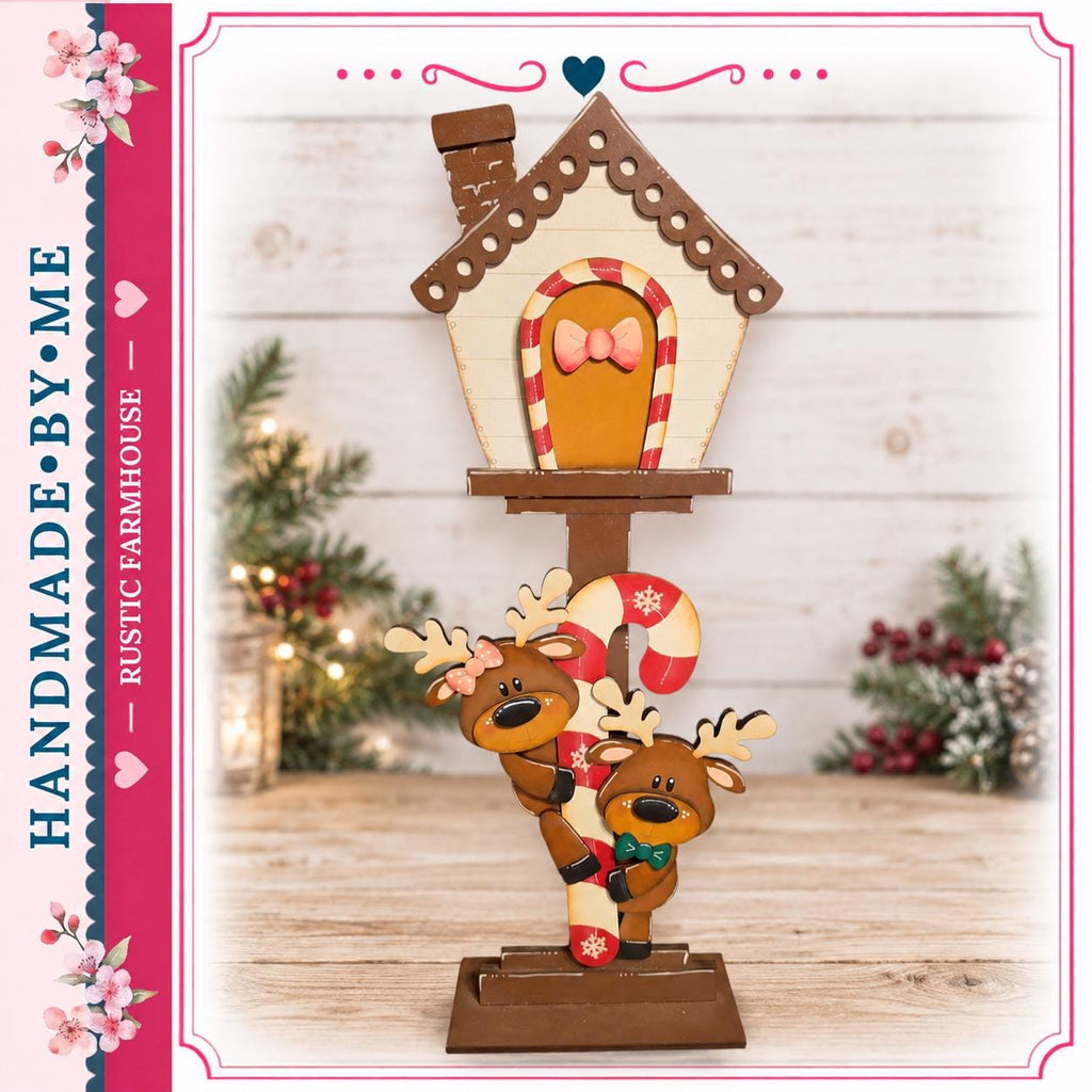 A hand-made wooden mailbox with a gingerbread house and reindeer decorations, set against a backdrop of Christmas trees and holiday decorations.